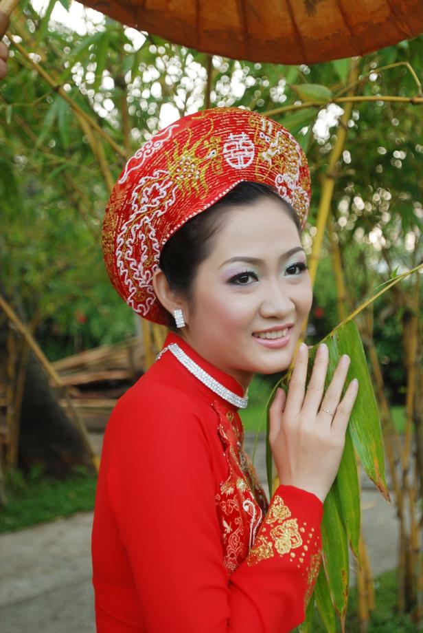 Eine junge Frau in traditioneller vietnamesischer Kleidung und Kopfbedeckung lächelt.