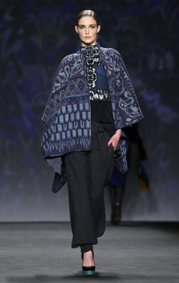 Ein Model präsentiert einen gemusterten Cape-Mantel und weite Hosen auf dem Laufsteg.