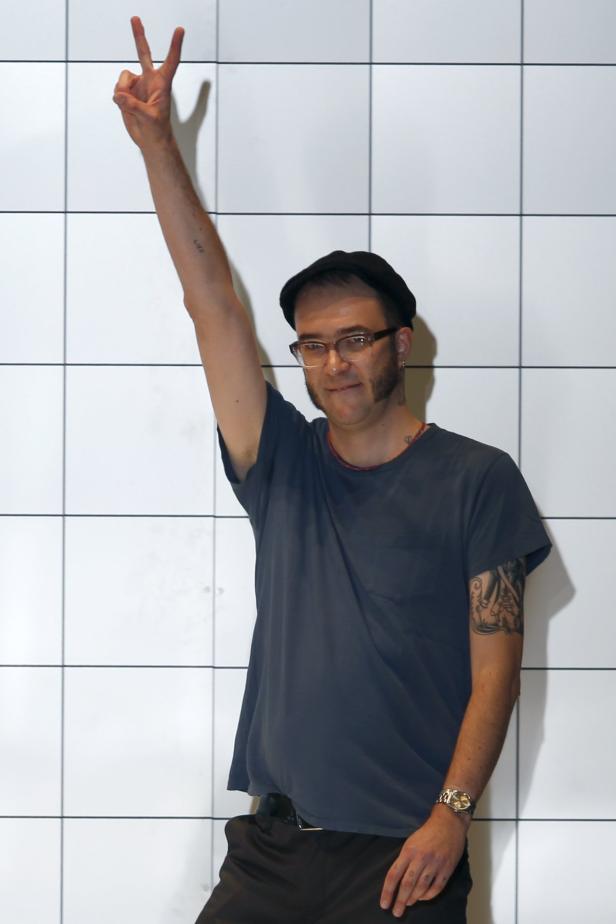 Ein Mann mit Brille und Bart hält seine Hand mit dem Victory-Zeichen hoch.