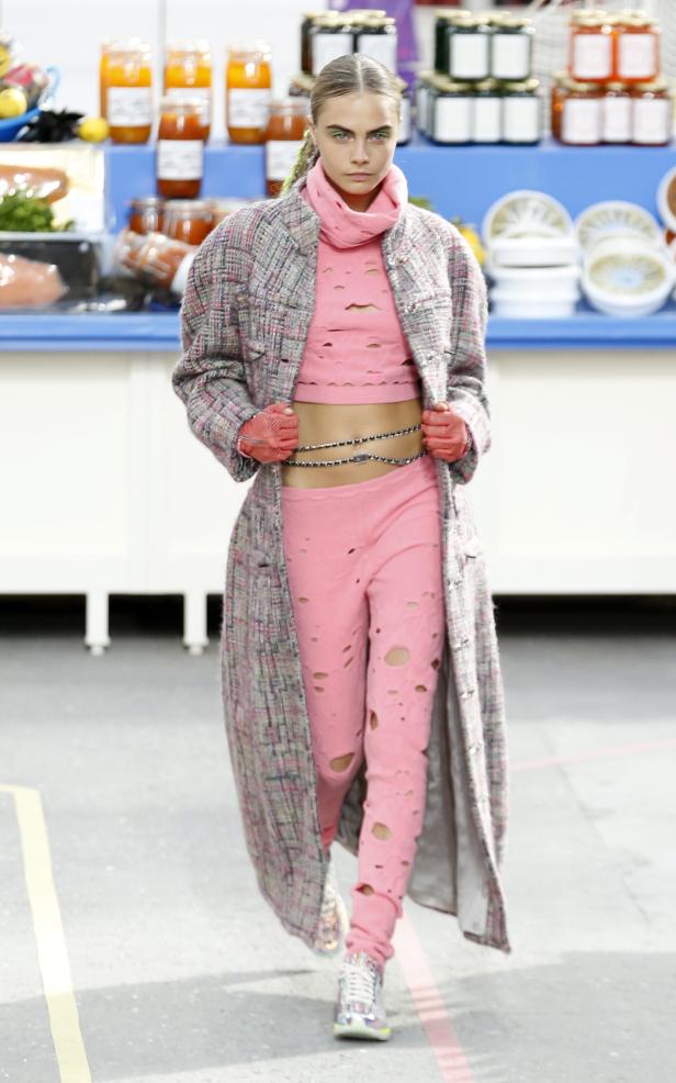 Cara Delevingne läuft in einem rosa Outfit und einem langen Mantel über einen Laufsteg.