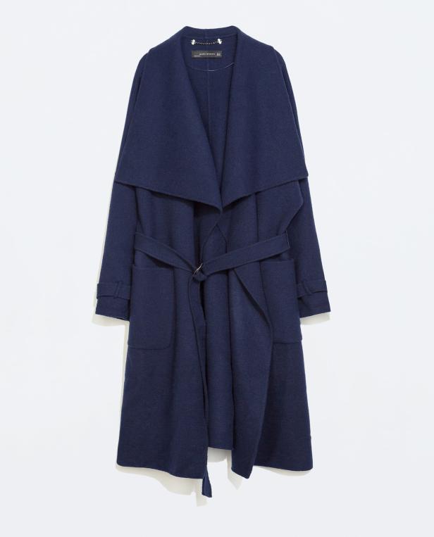 Ein marineblauer Mantel mit Gürtel hängt vor einem weißen Hintergrund.