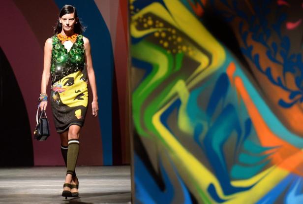 Eine Frau in einem bunten Kleid mit Gesichtsmotiv auf einem Laufsteg.