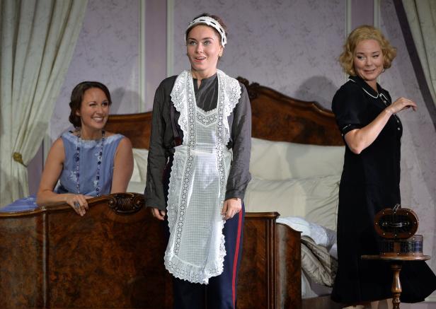 Drei Frauen stehen in einem Schlafzimmer, möglicherweise bei einer Theateraufführung.