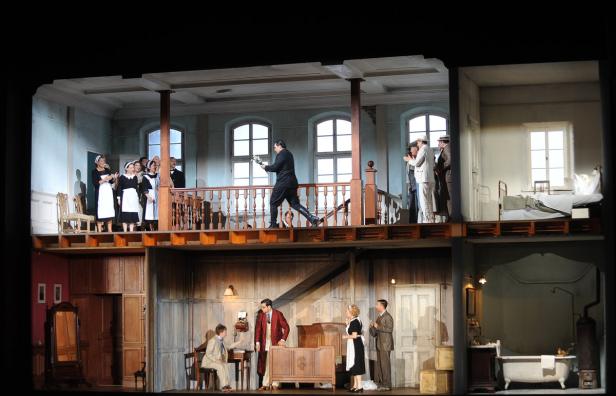 Bühnenbild einer Theateraufführung mit mehreren Räumen und Darstellern.