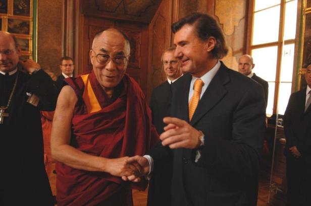 Der Dalai Lama schüttelt einem Mann im Anzug die Hand.