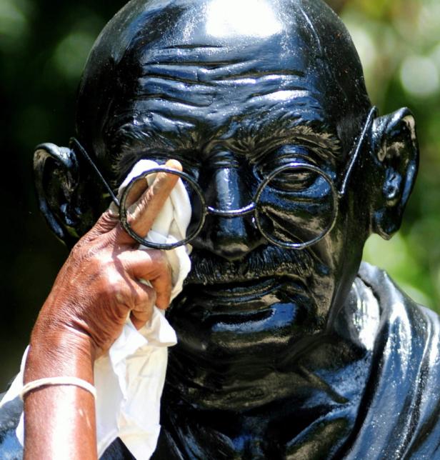 Eine Person putzt die Brille einer Gandhi-Statue mit einem Tuch.