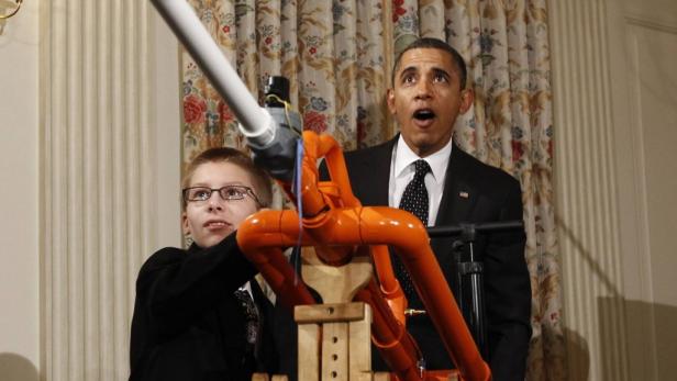 Ein Junge bedient eine Apparatur, während Barack Obama überrascht daneben steht.