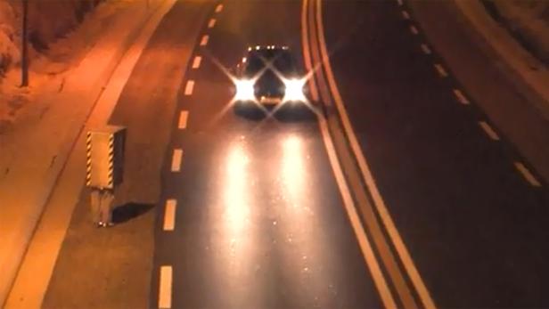 Ein Auto fährt nachts auf einer Straße mit einem Blitzer am Straßenrand.