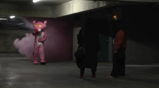 Eine Person im Kostüm des rosaroten Panthers steht in einer Tiefgarage und raucht.