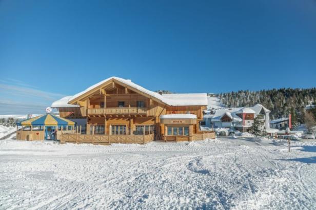 Ein hölzernes Chalet mit Schnee auf dem Dach an einem sonnigen Wintertag.