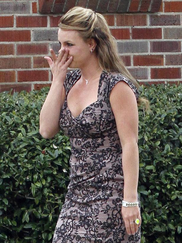Britney Spears mit einem Spitzenkleid vor einer grünen Hecke.