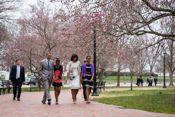 Die Familie Obama geht auf einem Weg entlang, gesäumt von blühenden Bäumen.