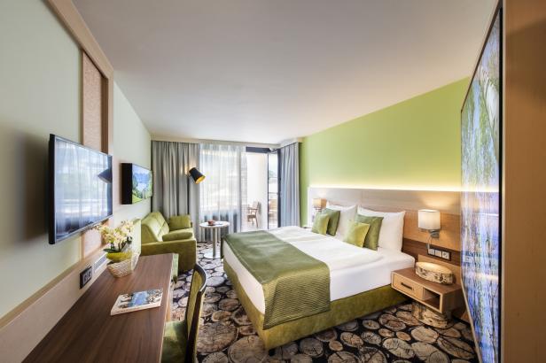 Ein helles Hotelzimmer mit Doppelbett, Sofa und Balkon.