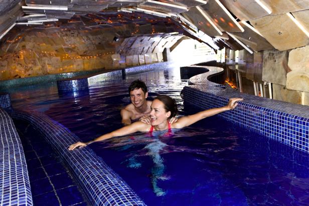 Ein lächelndes Paar entspannt sich in einem blau gefliesten Innenpool.