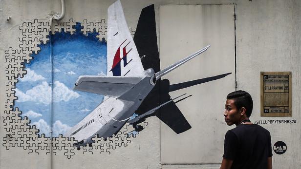 Ein Mann betrachtet ein Wandgemälde eines Flugzeugs der Malaysia Airlines, umgeben von Puzzleteilen.