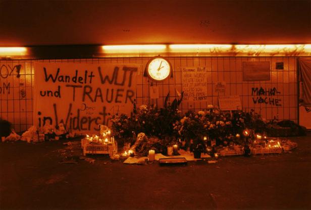Eine Gedenkstätte mit Blumen, Kerzen und Graffiti-Botschaften wie „Wandelt Wut und Trauer in Widerstand“.