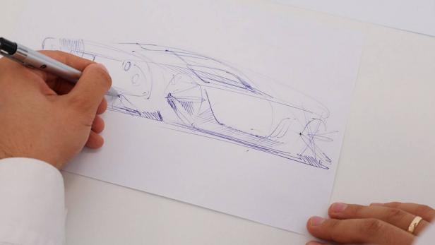 Eine Hand zeichnet mit einem Stift eine Skizze eines Autos auf ein Blatt Papier.