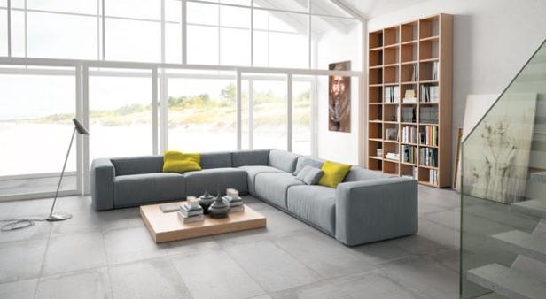 Ein modernes Wohnzimmer mit grauer Couch, Holztisch und großem Fenster mit Blick auf den Strand.