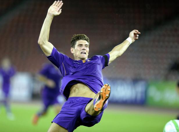 Ein Fußballspieler in lila Trikot springt und schießt den Ball.