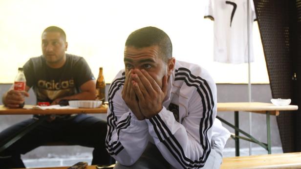 Zwei Männer schauen angespannt ein Fußballspiel, einer verdeckt sein Gesicht mit den Händen.