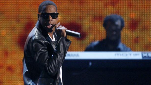 Jay-Z tritt in einer schwarzen Lederjacke und Sonnenbrille auf einer Bühne auf.