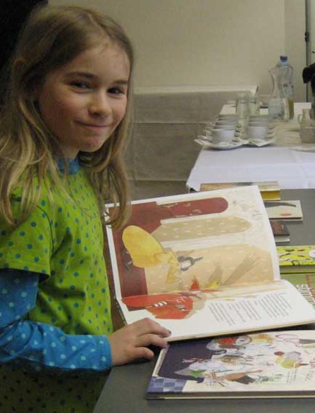 Ein junges Mädchen liest ein Bilderbuch an einem Tisch.
