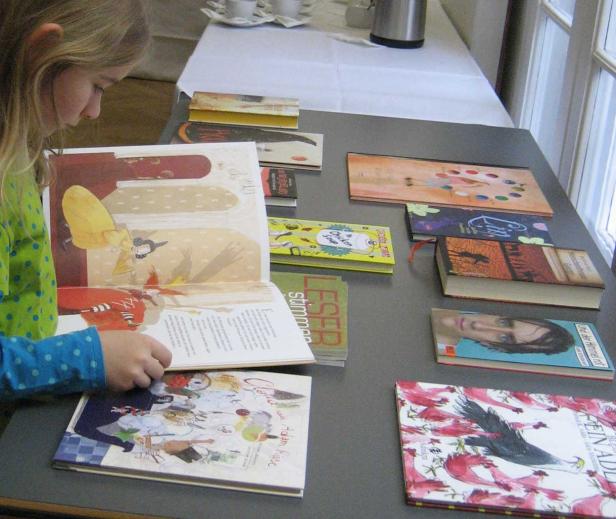 Ein Mädchen liest ein Bilderbuch an einem Tisch voller Bücher.