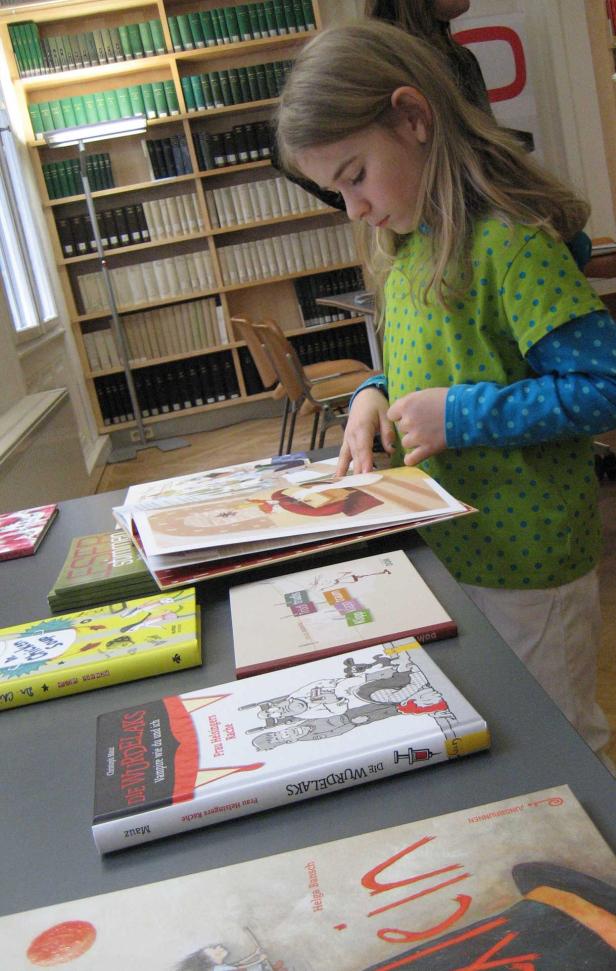 Ein Mädchen steht an einem Tisch in einer Bibliothek und blättert in einem Buch.