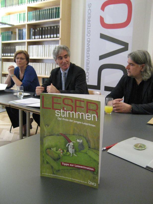 Drei Personen sitzen an einem Tisch mit dem Buch „Leserstimmen“ im Vordergrund.