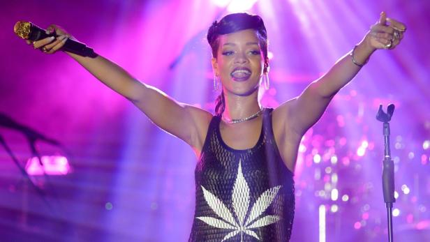 Rihanna tritt mit erhobenen Armen und einem Mikrofon in der Hand auf einer Bühne auf.