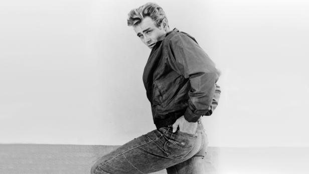 James Dean posiert in Jeans und Jacke, den Blick über die Schulter gerichtet.