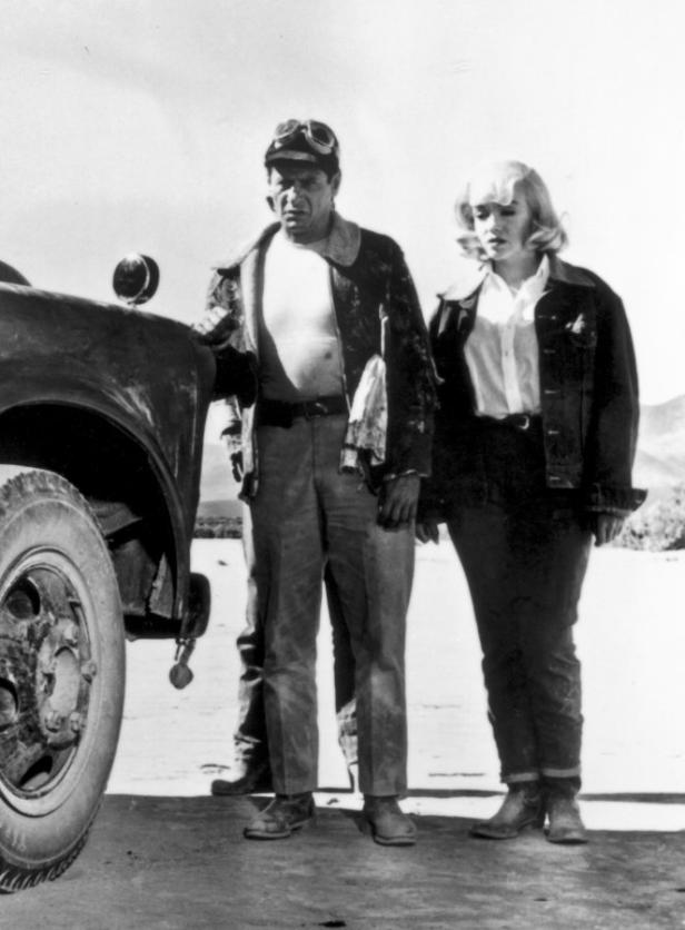 Ein Mann mit Schutzbrille und eine Frau stehen neben einem alten Auto.