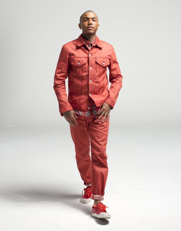 Ein tätowierter Mann in einem roten Denim-Anzug und roten Turnschuhen geht auf einem weißen Hintergrund.