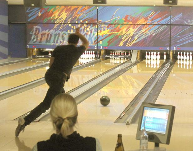 Ein Mann wirft eine Bowlingkugel auf eine Kegelbahn.