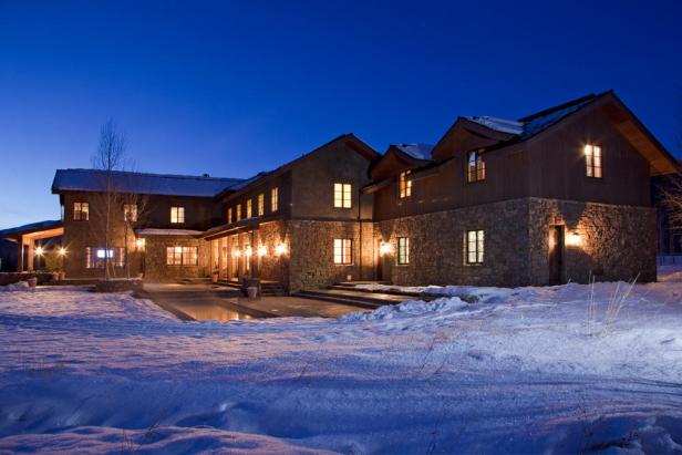 Ein großes, beleuchtetes Haus mit Steinmauern steht in einer verschneiten Landschaft.