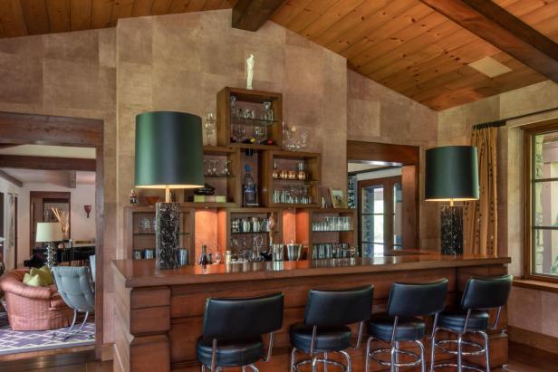 Eine Bar mit Barhockern und Regalen voller Gläser in einem Wohnzimmer.