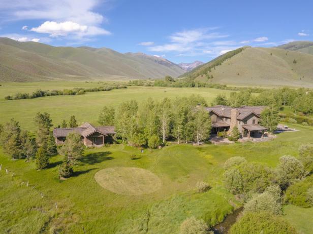 Luftaufnahme eines Hauses auf einem grünen Hügel mit Bergen im Hintergrund.