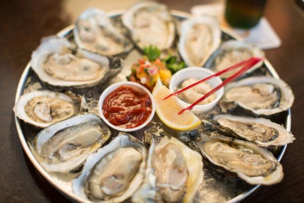 Ein Teller mit frischen Austern, serviert mit Zitrone und verschiedenen Dips.