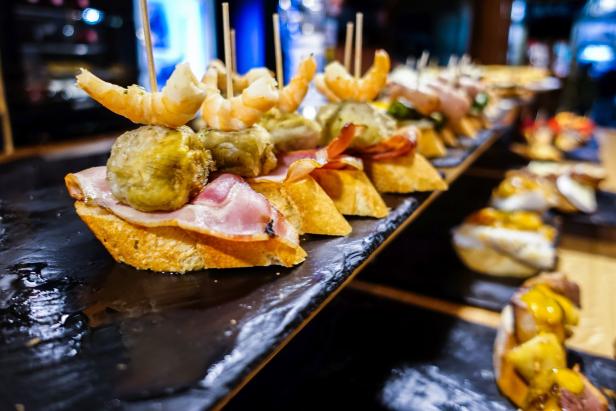 Eine Auswahl an Pintxos, belegte Brote mit verschiedenen Belägen, auf einer schwarzen Platte.