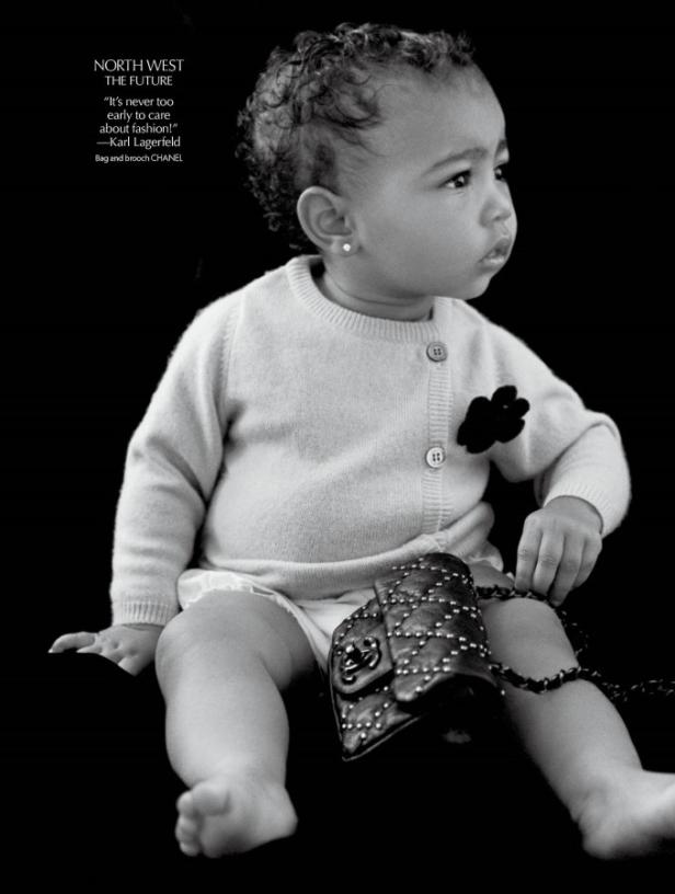 Ein Baby mit Ohrring, Cardigan und Chanel-Tasche posiert vor schwarzem Hintergrund.