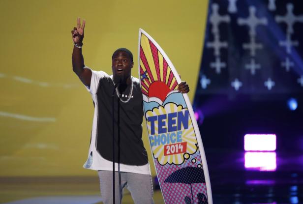 Kevin Hart hält ein Teen Choice Award Surfbrett hoch und zeigt das Victory-Zeichen.