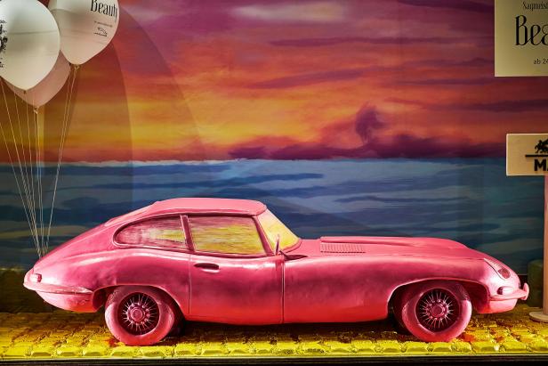 Ein rosafarbener Jaguar E-Type vor einem gemalten Sonnenuntergang und Ballons.