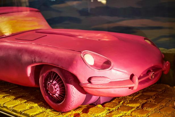 Ein rosafarbenes Jaguar E-Type Modell steht auf einem gelben Untergrund.