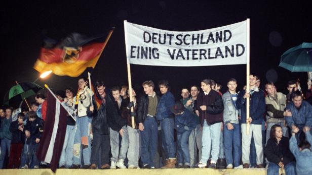 Eine Menschenmenge hält eine Deutschlandflagge und ein Transparent mit der Aufschrift „Deutschland einig Vaterland“.