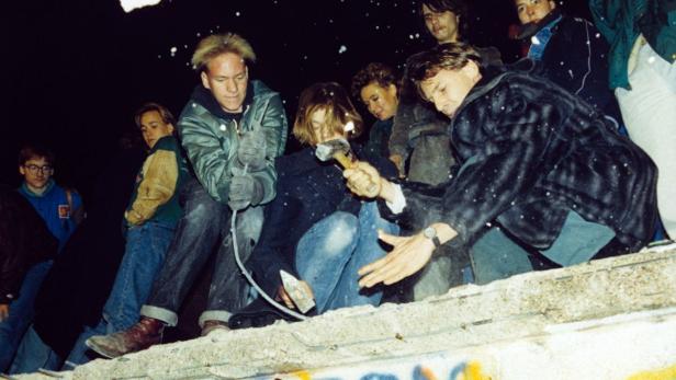 Menschen schlagen mit Hämmern auf die Berliner Mauer ein.