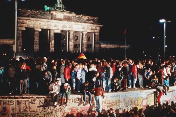 Menschen feiern an der Berliner Mauer vor dem Brandenburger Tor.