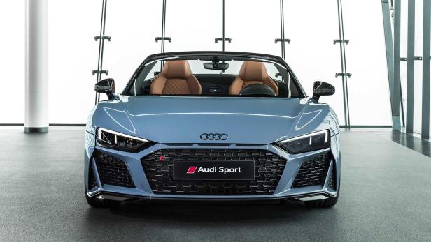 Ein blauer Audi R8 Spyder mit braunen Ledersitzen steht in einem Ausstellungsraum.
