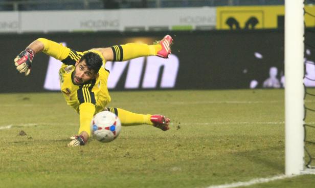 Ein Torwart in gelber Sportkleidung wehrt einen Fußball ab.