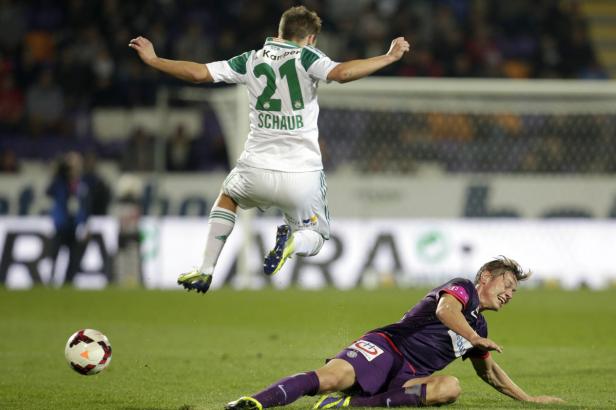 Ein Fußballspieler springt über einen am Boden liegenden Gegenspieler.
