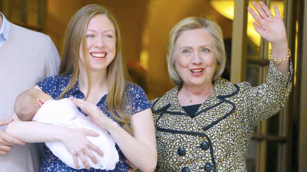 Chelsea Clinton hält ihr Baby, während Hillary Clinton lächelt und winkt.